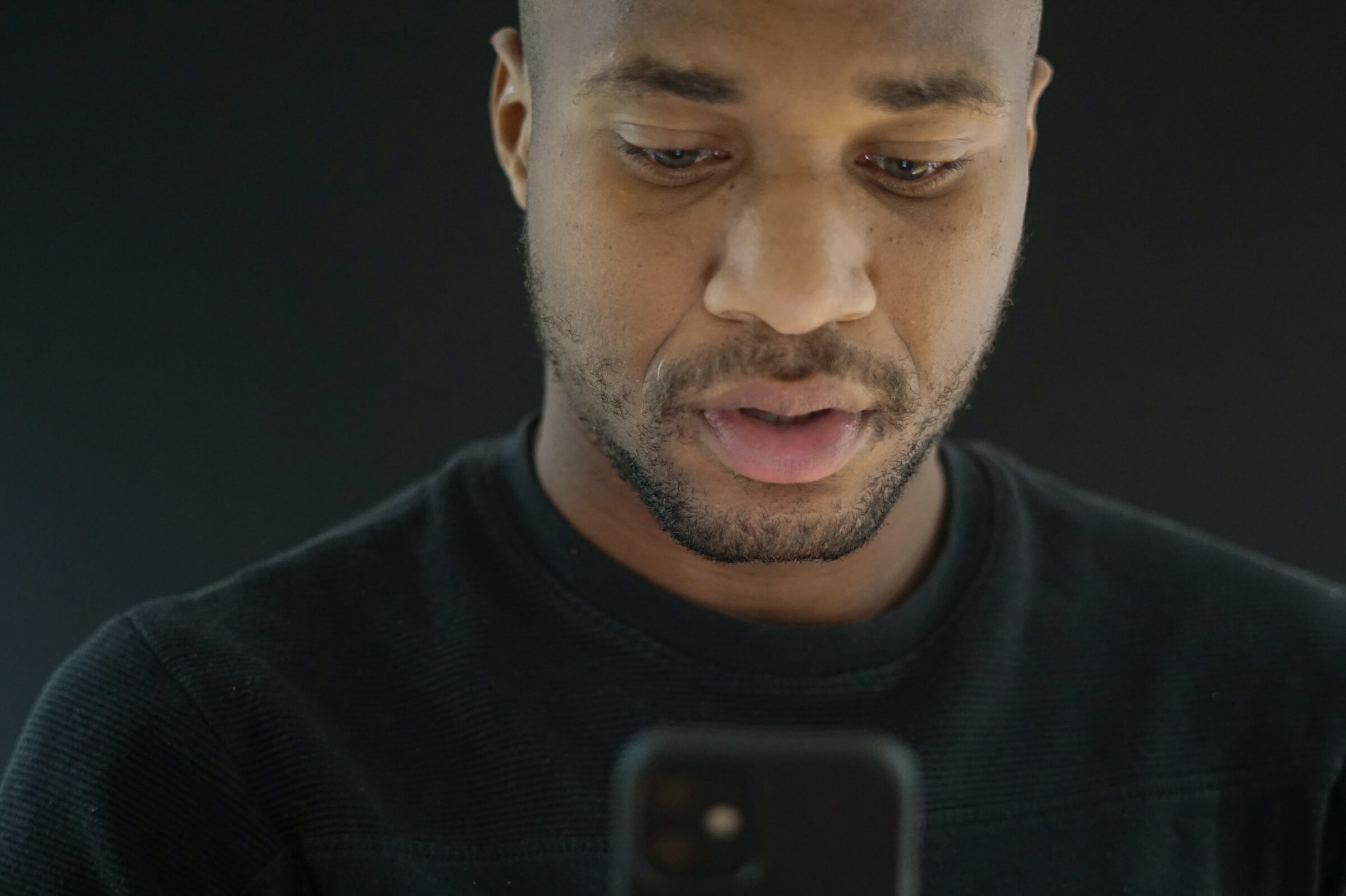 Close-up of a man looking down at his phone, thinking about his spending